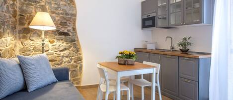 A cozy kitchen with a stone wall, a wooden dining table with chairs, and grey cabinets.