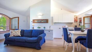 Una sala de estar moderna con un sofá azul, una mesa de comedor con sillas y una zona de cocina con armarios blancos.