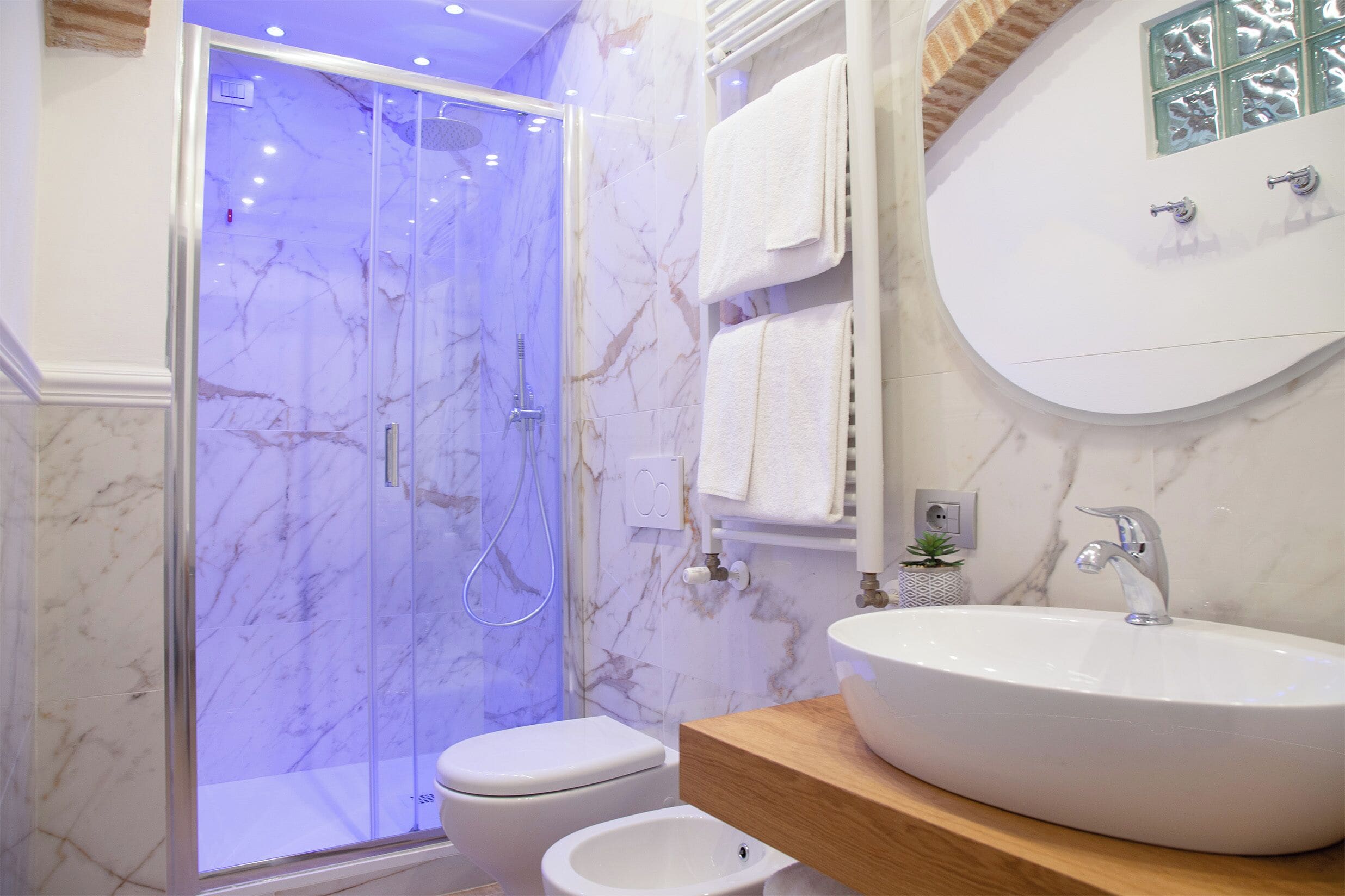 Un bagno con doccia vetrata, lavandino bianco e parete rivestita in marmo.