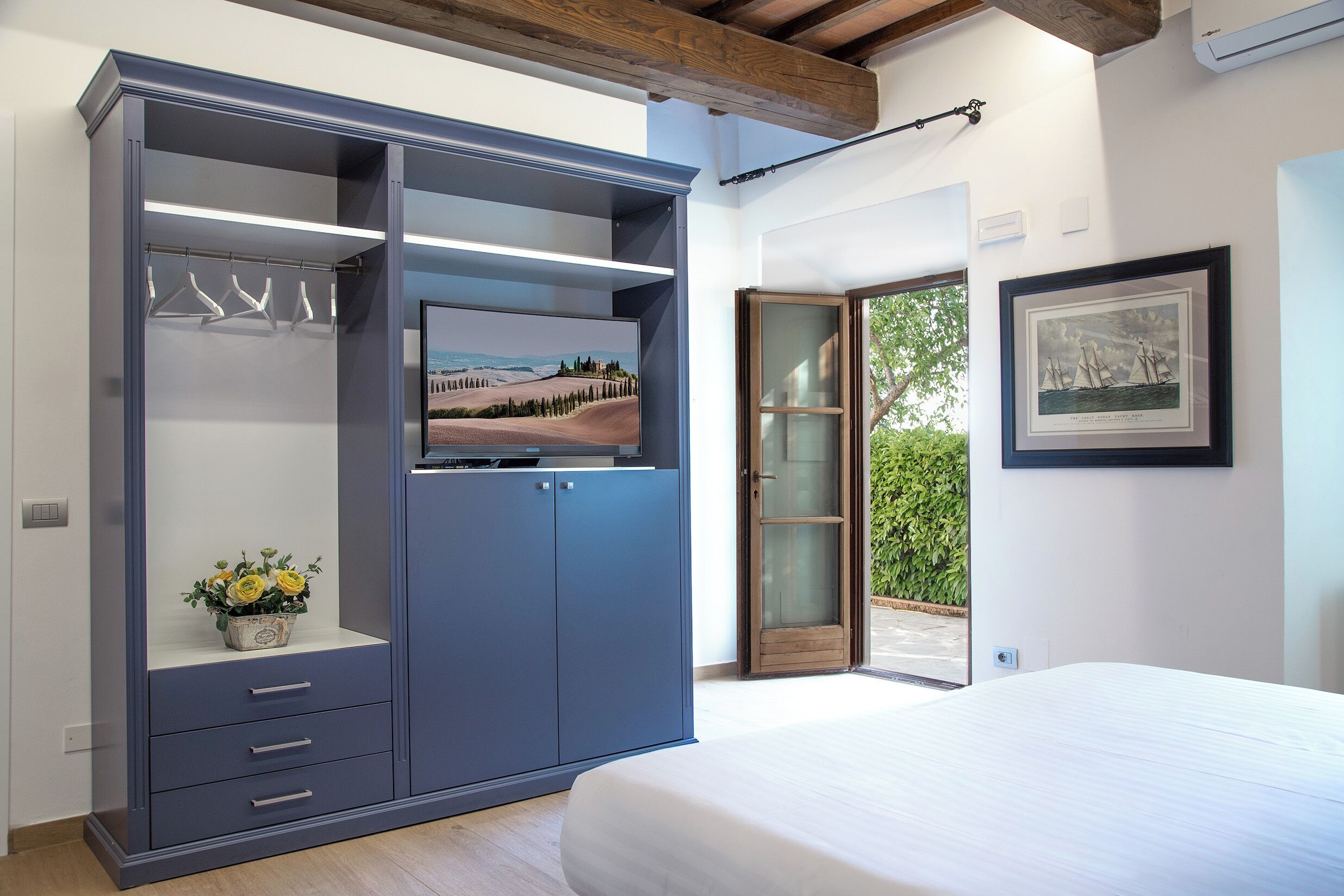 A bedroom with a bed, a wardrobe, a painting, and a view of greenery.