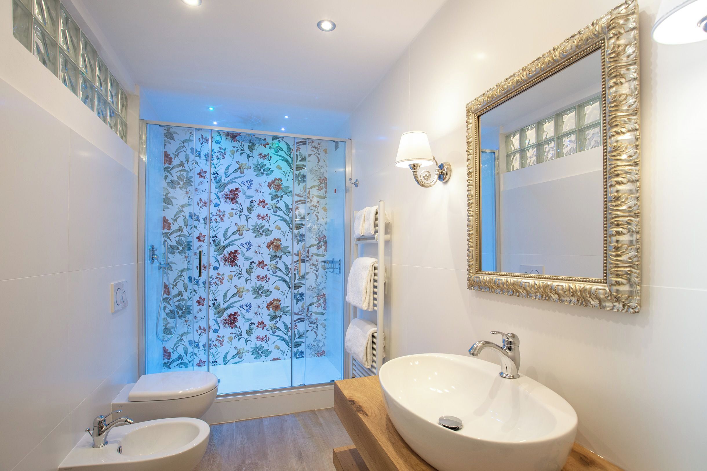 Une salle de bain dotée d’une douche à parois de verre, d’un lavabo, de toilettes et d’un miroir encadré d’un cadre orné.