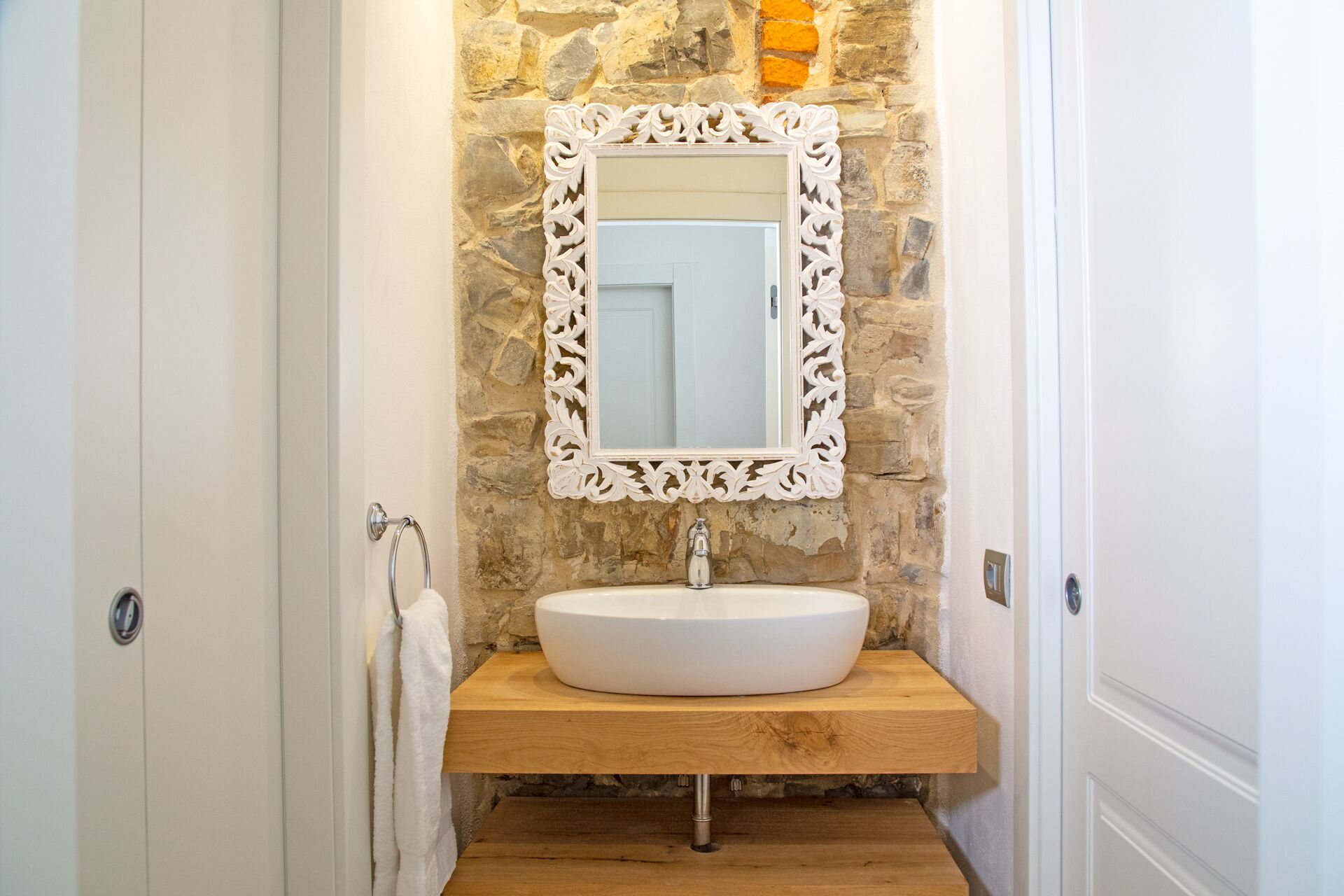 A bathroom with a stone wall, a white sink, and a decorative mirror frame.