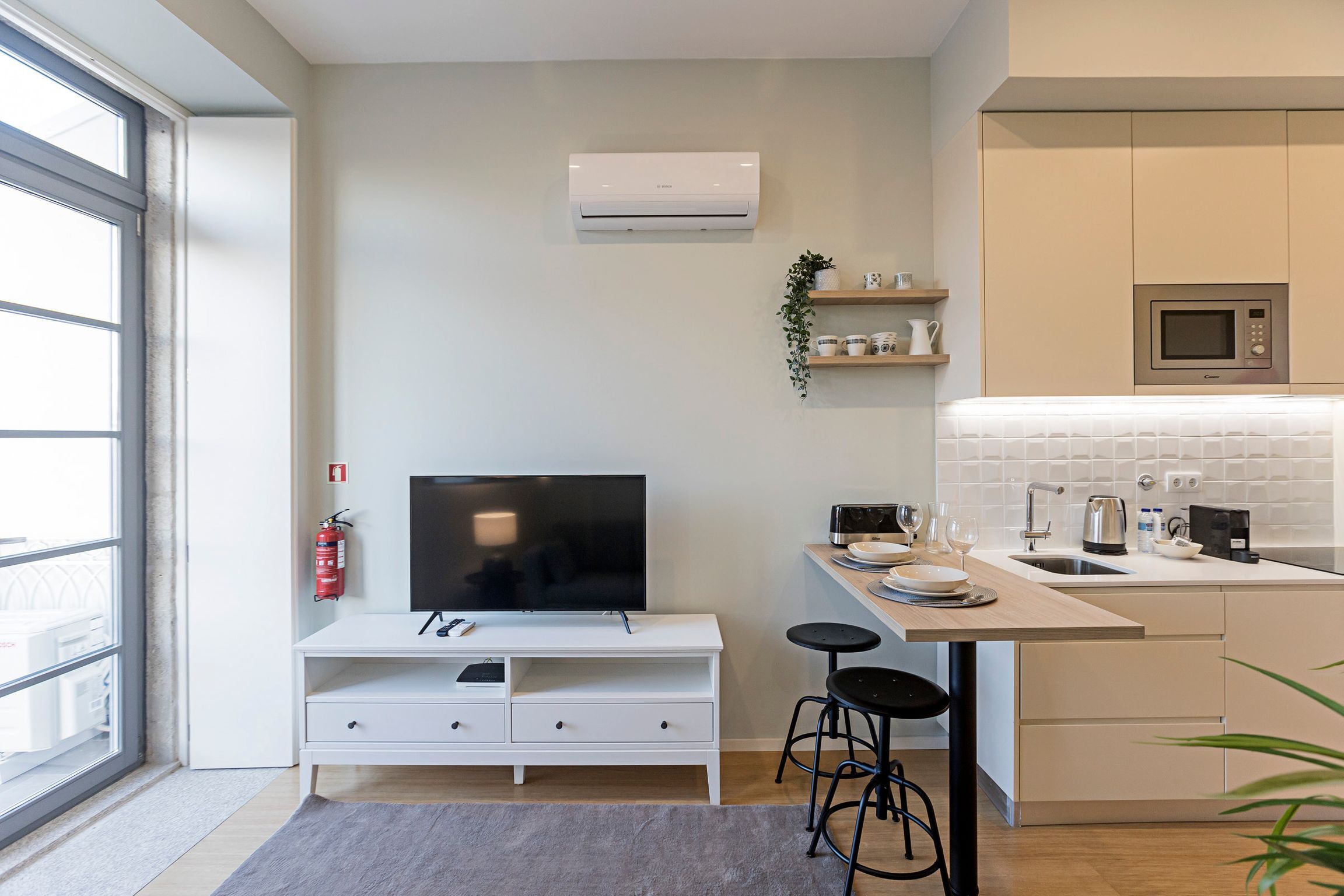 Een moderne keuken met een ingebouwde magnetron, een klein eethoekje met krukken en een groot raam voor natuurlijk licht.