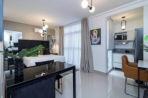 A modern hotel room with a bed, a desk with a chair, a dining table, and a kitchenette. - NoMa Work & Travel - 2C (Centro)