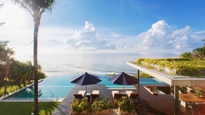 A poolside area with lounge chairs and umbrellas overlooking a clear blue sea. - The Ungasan Clifftop Resort (Pecatu)