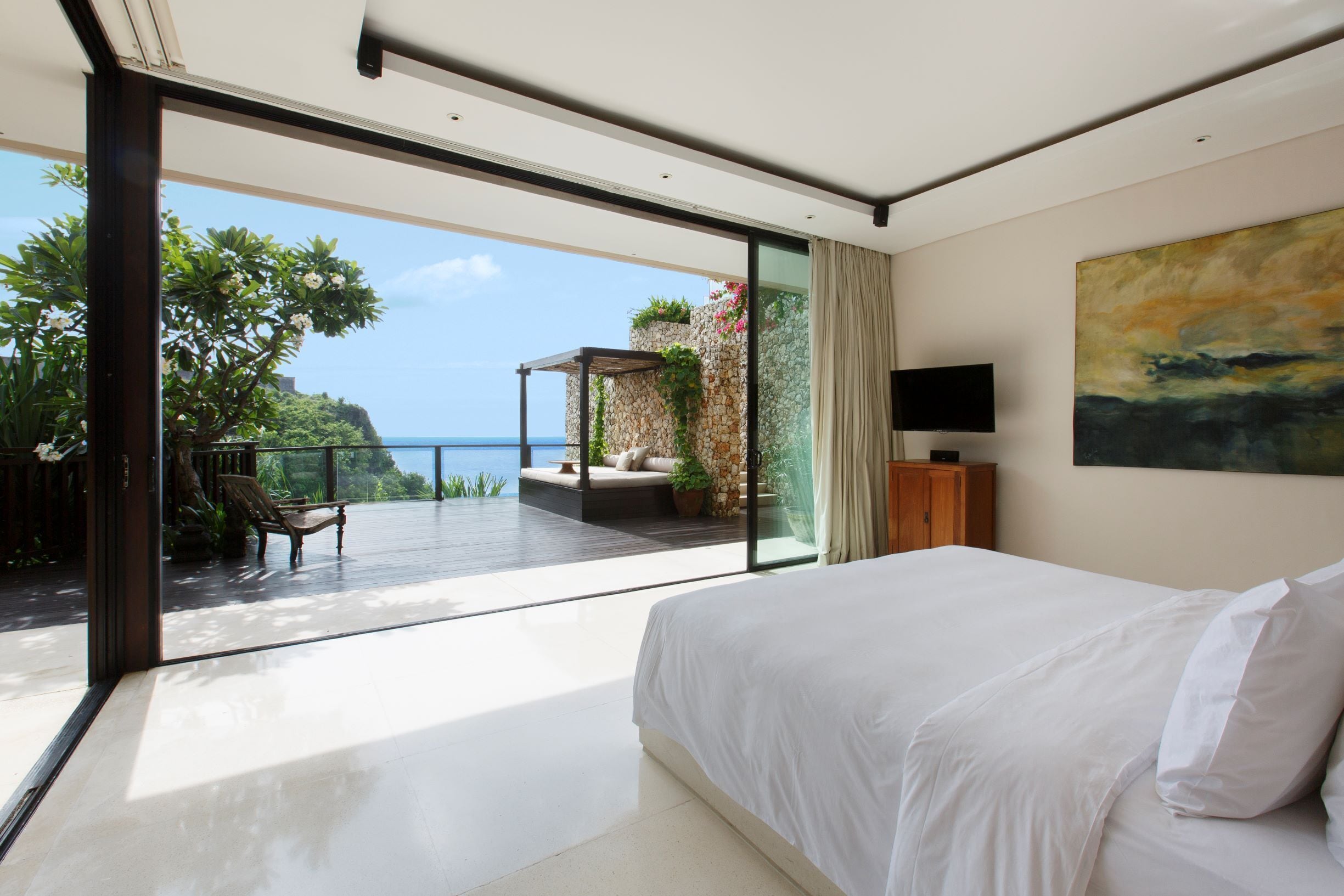 A bedroom with a large bed, a TV, and a view of the ocean.