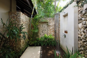 A stone-walled outdoor area with a wooden deck, a decorative wall panel, and a white door. - The Ungasan Clifftop Resort (Pecatu)