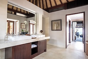 A modern bathroom with a large vanity, two sinks, and a large mirror. There is a wooden cabinet below the vanity and a framed artwork on the wall. - The Ungasan Clifftop Resort (Pecatu)