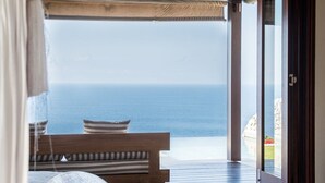 A bedroom with a large bed, a wooden bench, and a view of the sea through an open door. - The Ungasan Clifftop Resort (Pecatu)