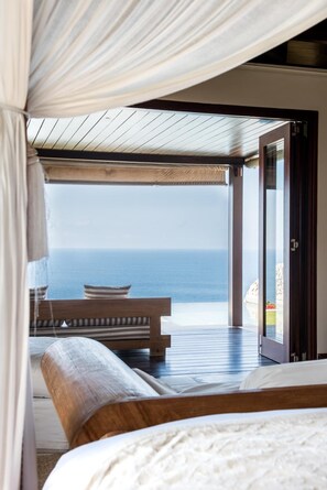 A bedroom with a large bed, a view of the ocean, and a wooden deck. - The Ungasan Clifftop Resort (Pecatu)