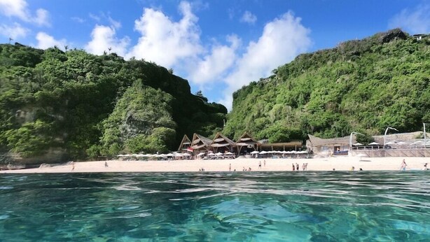 A beach with clear turquoise water, a sandy shore, and a row of thatched-roof huts. - The Ungasan Clifftop Resort (Pecatu)