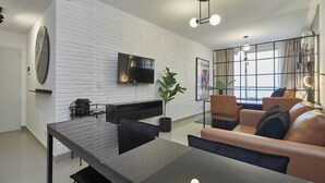 Un salon moderne avec une table à manger noire, un canapé en cuir et un grand téléviseur fixé sur un mur en briques blanches.