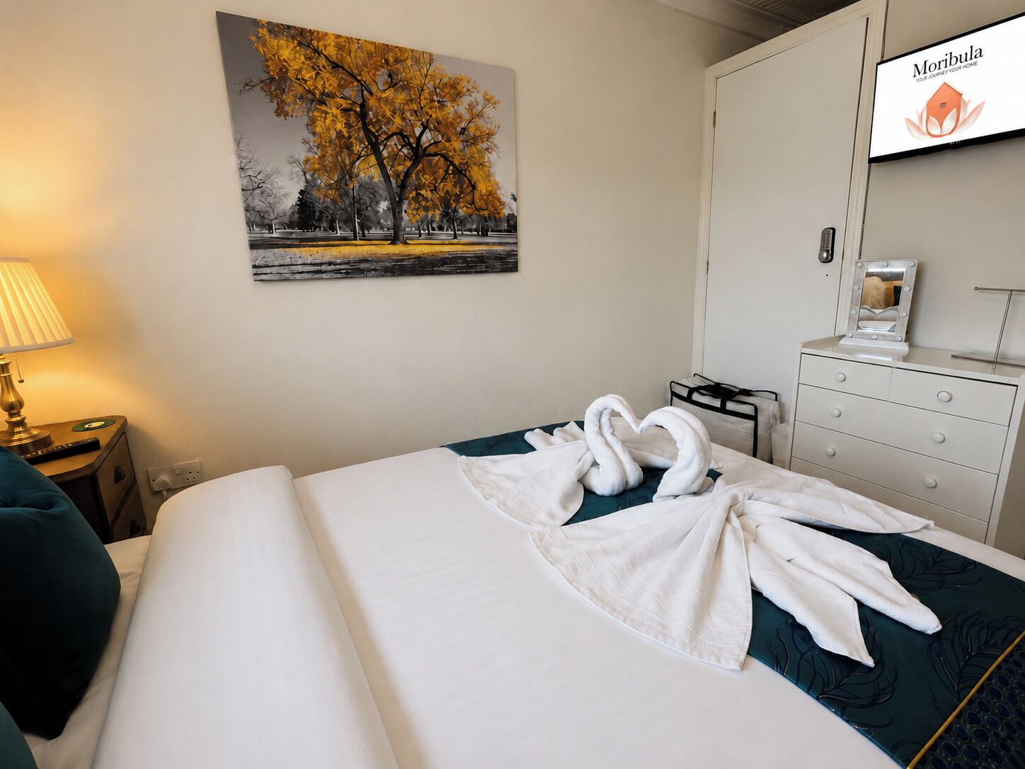 Une chambre d’hôtel avec un lit, un tableau représentant des arbres, une télévision et une commode.