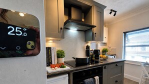 A modern kitchen with a digital thermometer, a stove, and a window with blinds. - Central Bedford Apartment | Secure Parking | Fast Wi-Fi | Walk to Station (Bedford)