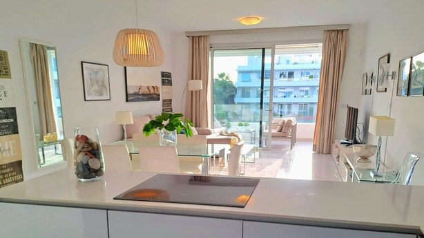 Ett modernt kök med en köksö i glas, en matplats med soffa och en balkong med utsikt över byggnaderna.