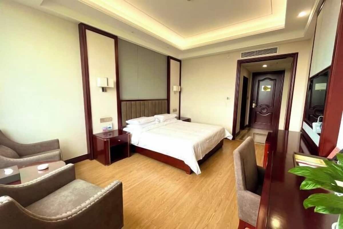 A hotel room with a bed, a desk, a chair, a nightstand, a mirror, and a plant.