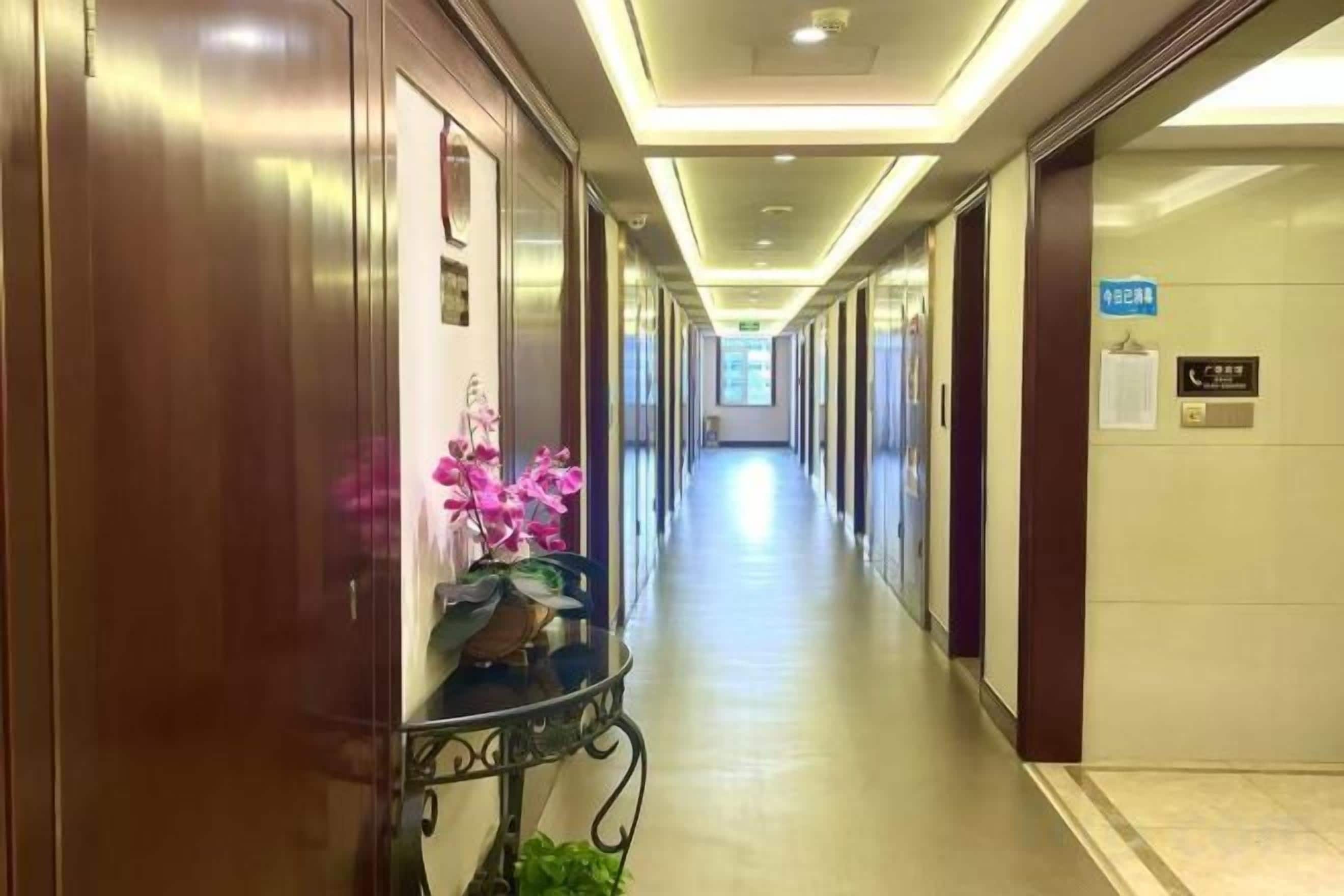 A hotel corridor with doors, a reception desk, and a sign indicating the elevator area.