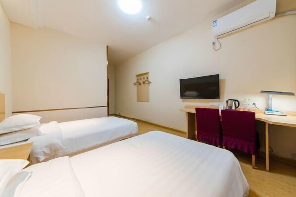 A hotel room with two single beds, a desk with a chair, a television, and an air conditioning unit.