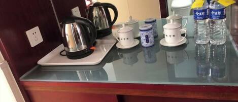 A hotel room's kitchenette with a kettle, teapot, cups, and bottled water on the counter.