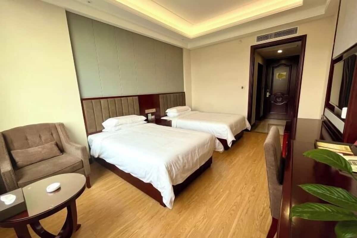 A hotel room with two beds, a sofa, a small table, and a plant.