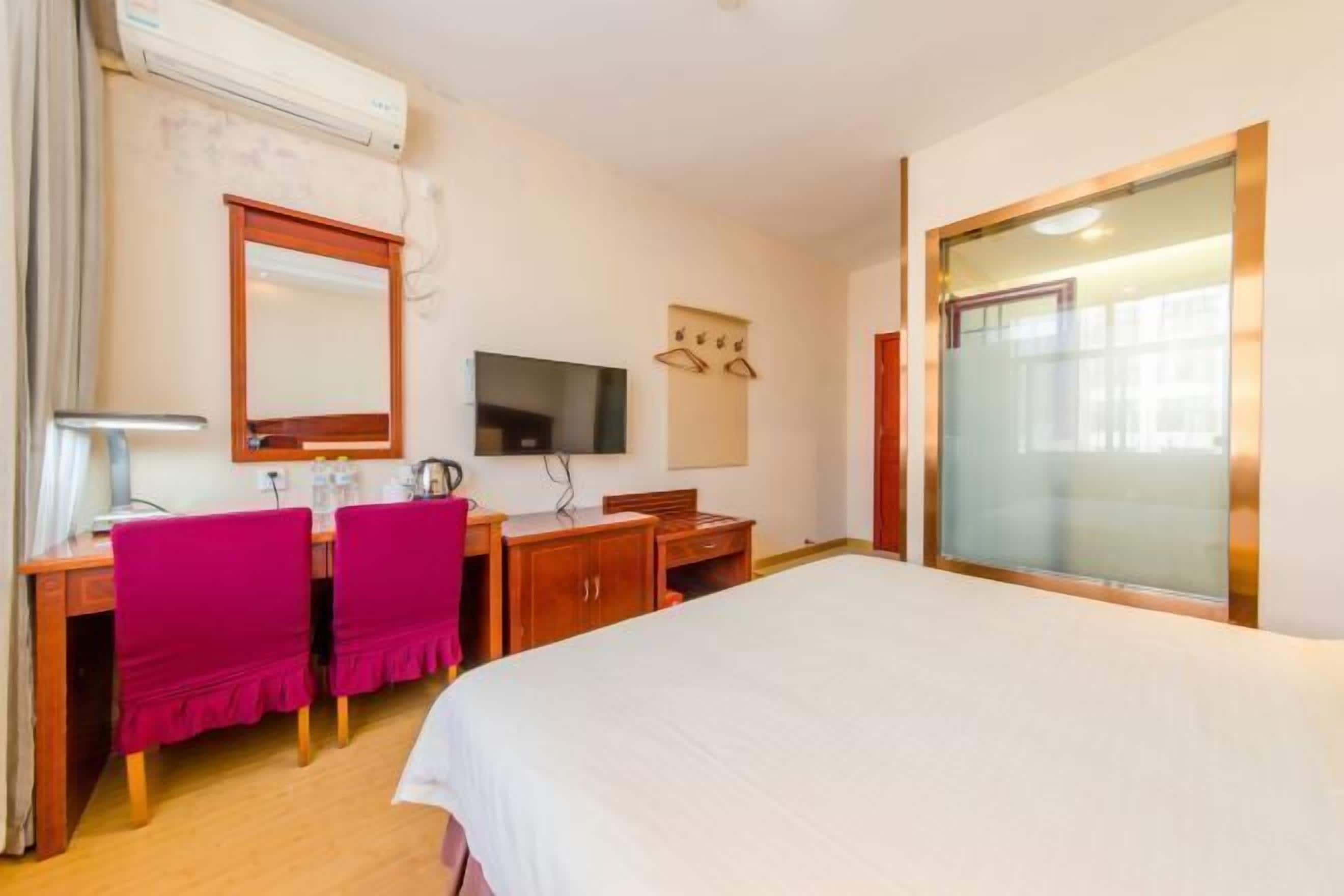 A hotel room with a bed, a desk with a chair, a television, and a window.