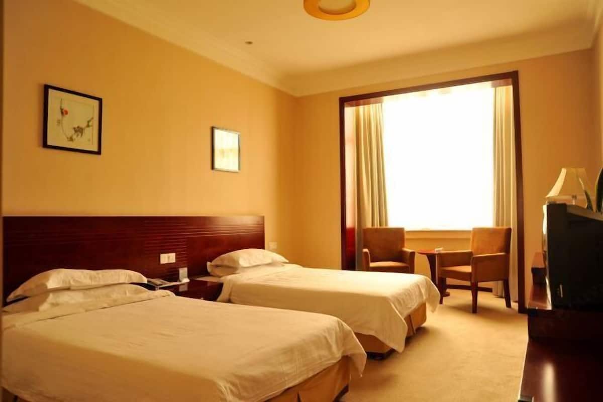 A hotel room with two single beds, a desk, a chair, and a television.
