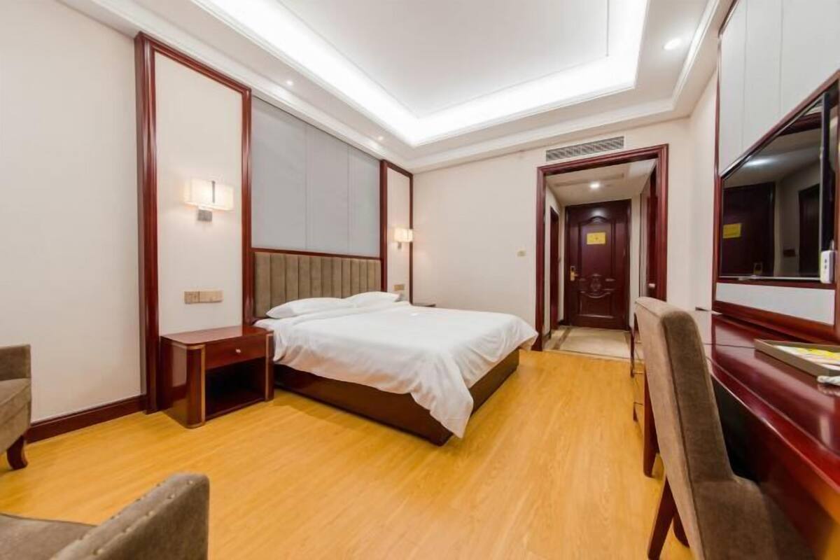 A hotel room with a bed, bedside table, chair, and a desk with a chair.