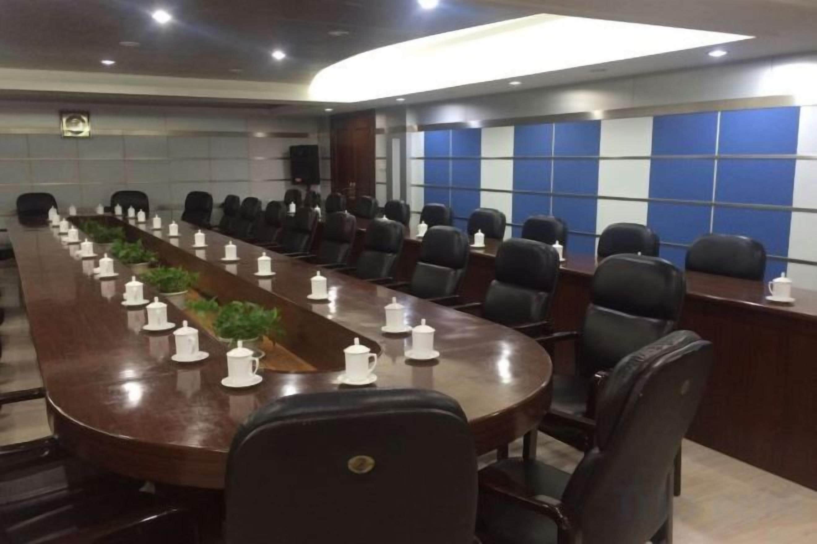 Une salle de conférence avec une longue table, de nombreuses chaises et un mur bleu orné d’un motif quadrillé.