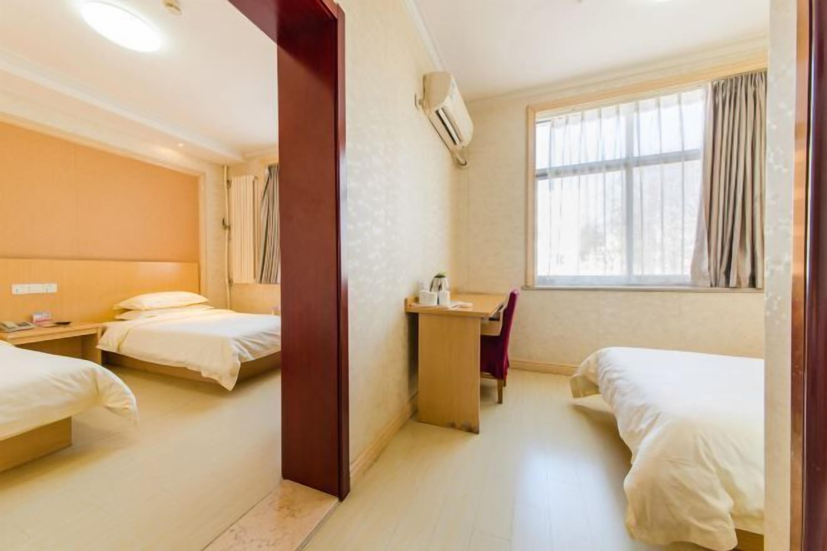 A hotel room with two single beds, a desk with a chair, and a window with curtains.