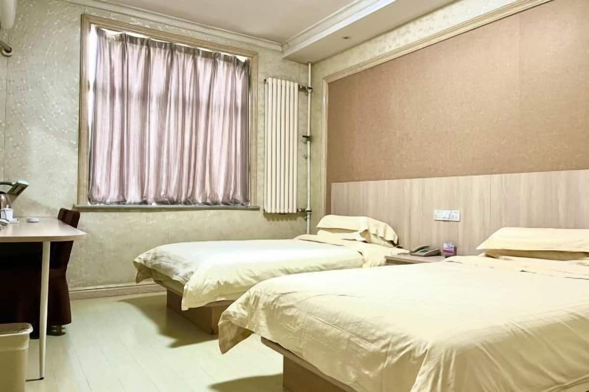 A hotel room with two single beds, a small table, and a window with curtains.