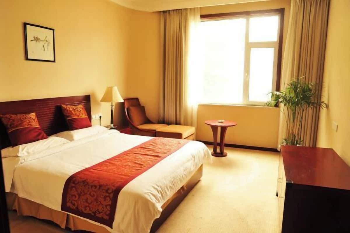 A hotel room with a large bed, a chair, a small table, and a window with curtains.