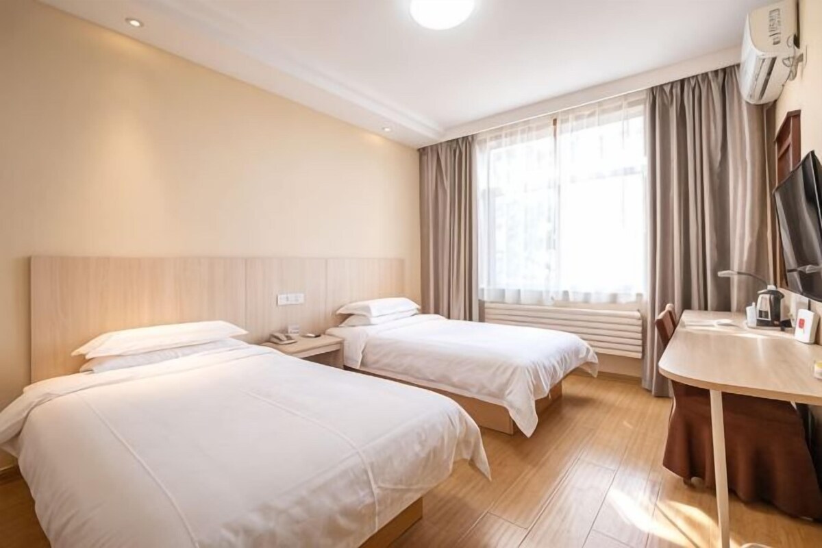 Habitación de hotel con dos camas, un escritorio y una ventana con cortinas.