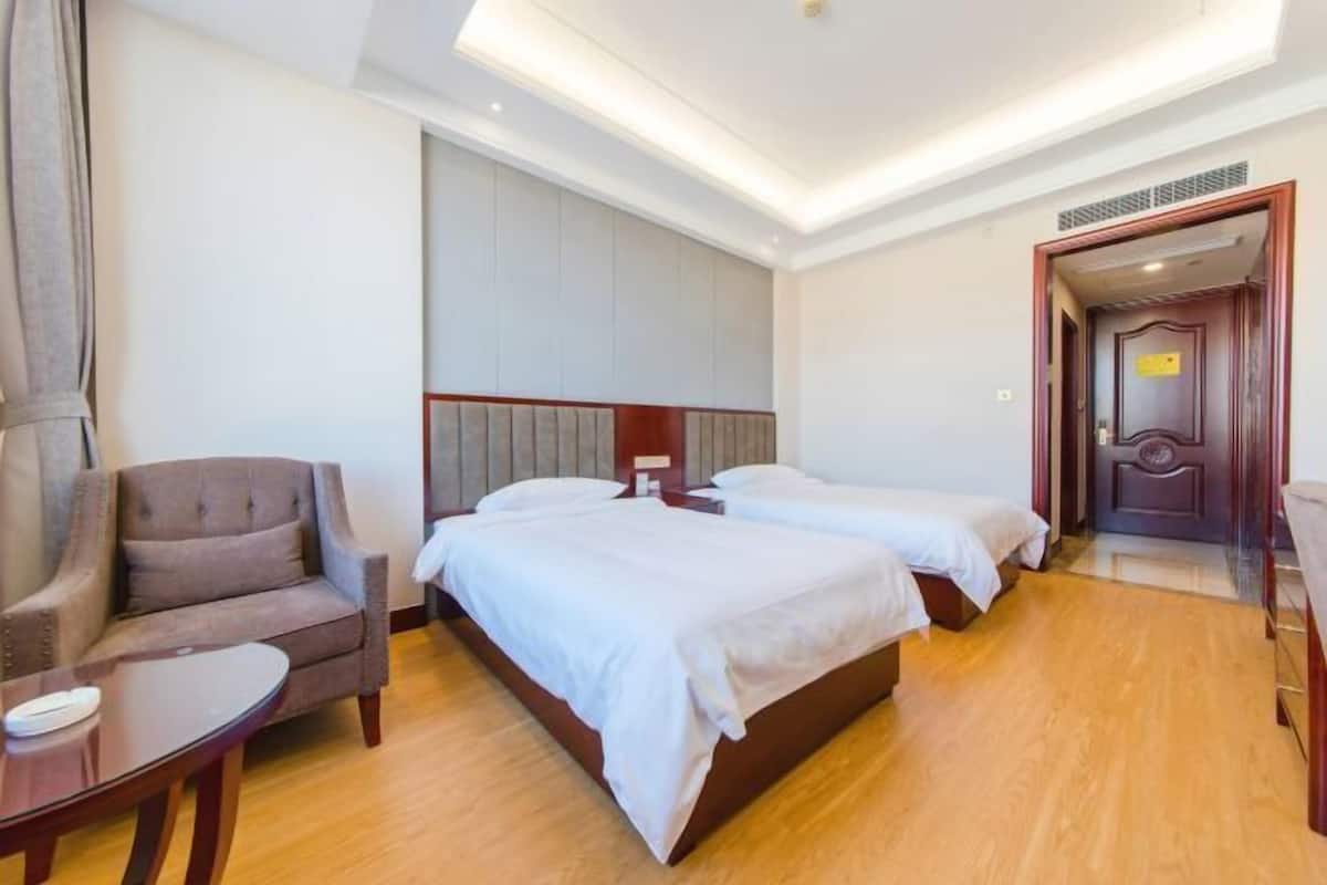 A hotel room with two beds, a chair, a small table, and a door.