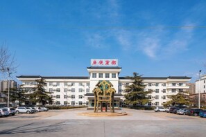 A hotel with a prominent sign, a parking lot, and a central decorative structure. - Guangrao Hotel (Guangrao)