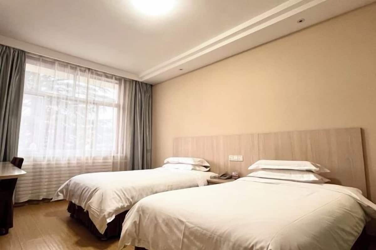 A hotel room with two beds, a desk, and a window with sheer curtains.
