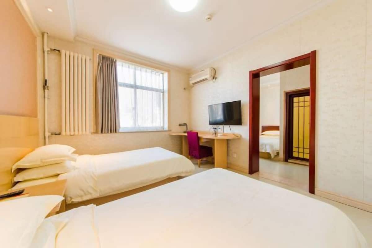 A hotel room with two single beds, a desk with a chair, a TV, and a large mirror.