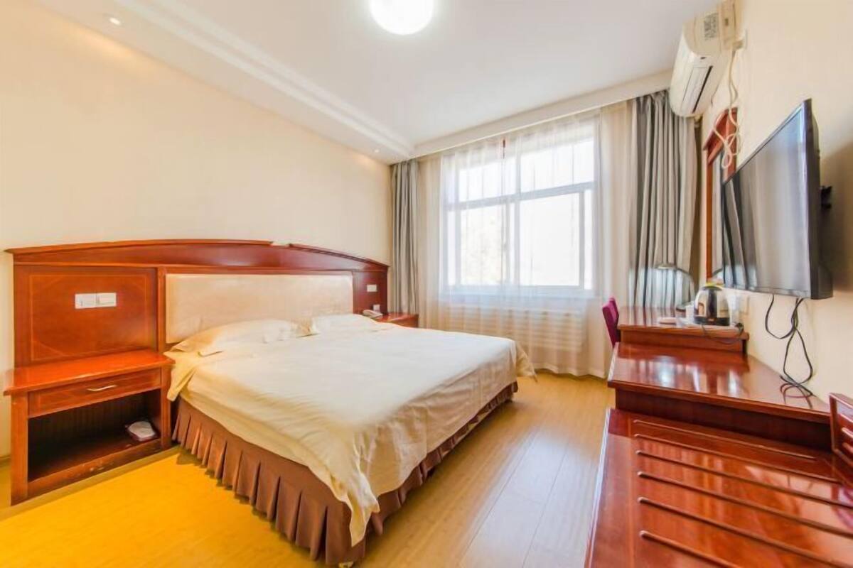 A hotel room with a large bed, a wooden desk, a television, and a window with curtains.