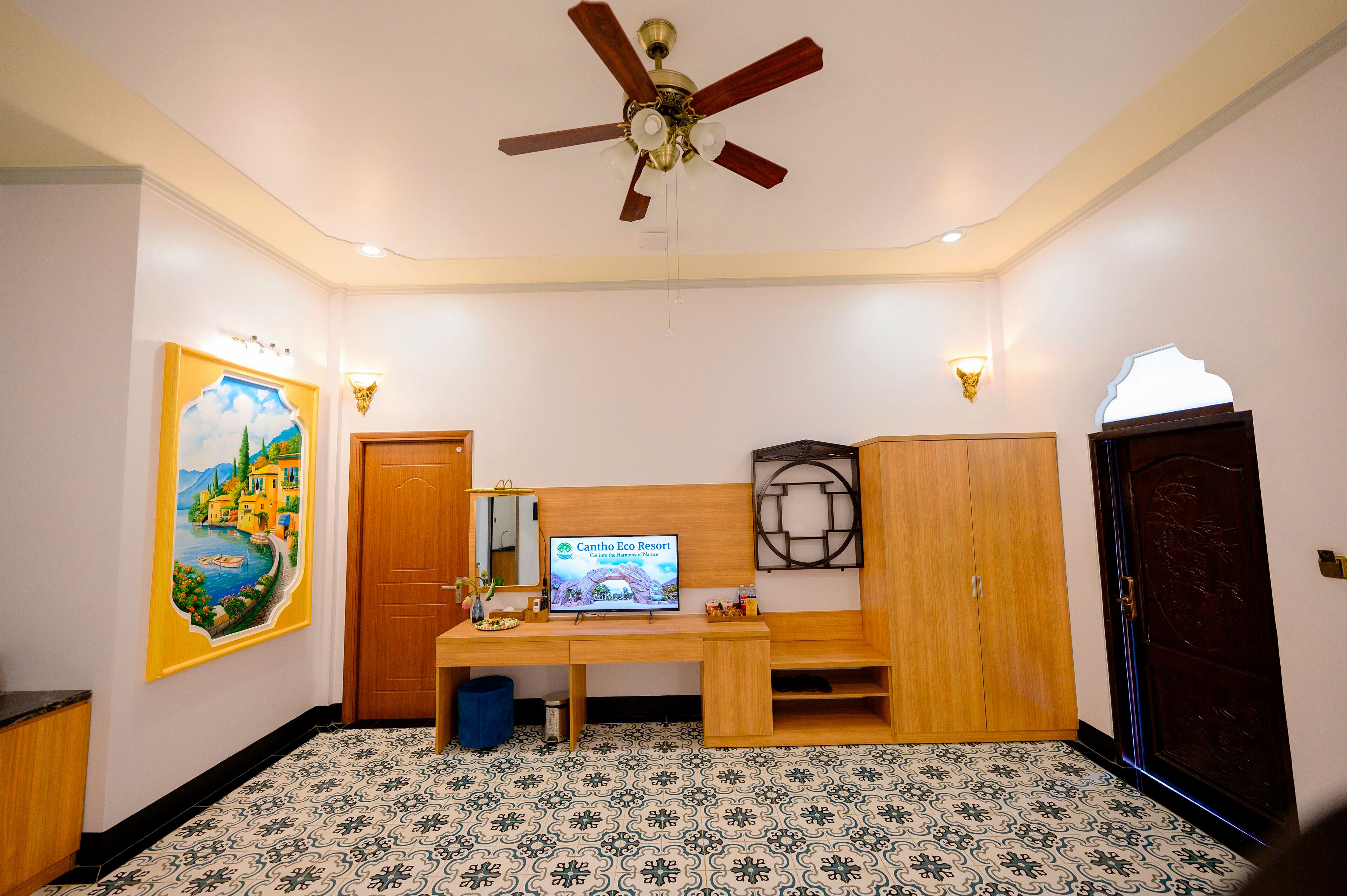 Een kamer met een plafondventilator, een bureau met een computerscherm, een schilderij aan de muur en een kamer met een vloer met een patroon.