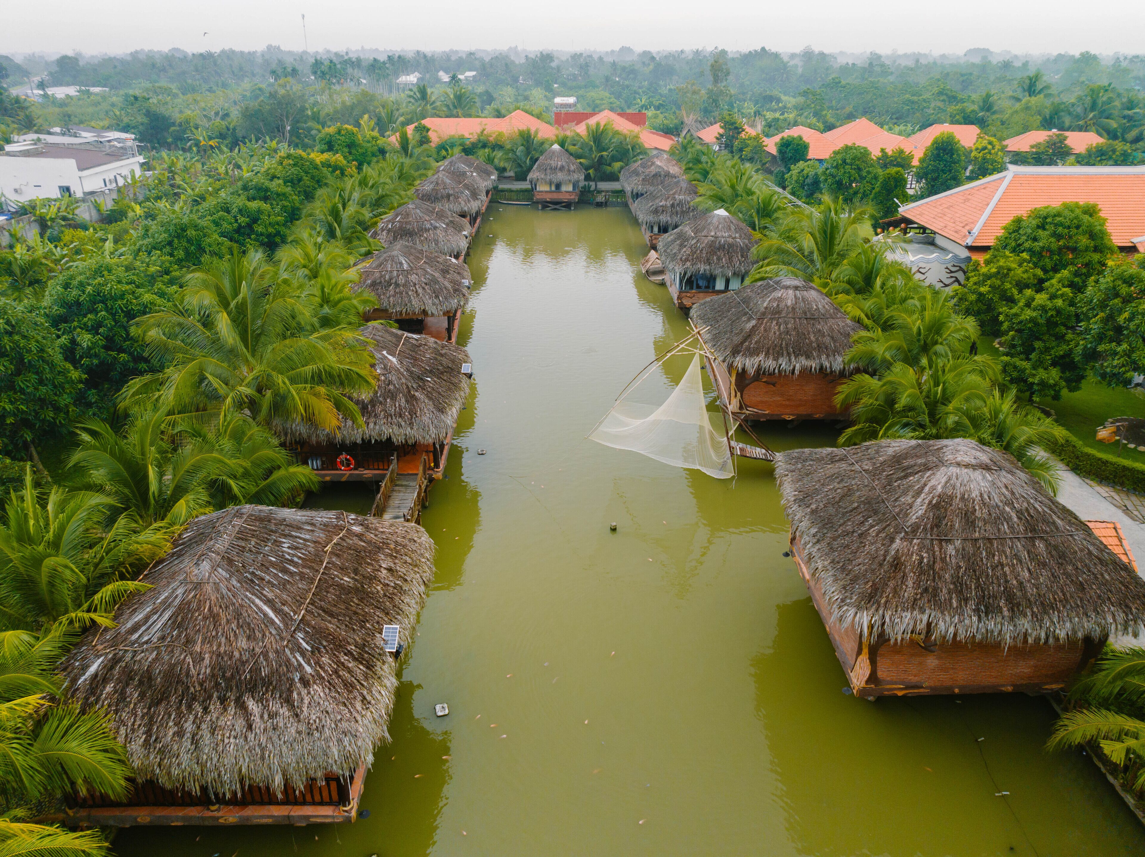 A waterway lined with thatched-roof huts, surrounded by lush greenery.