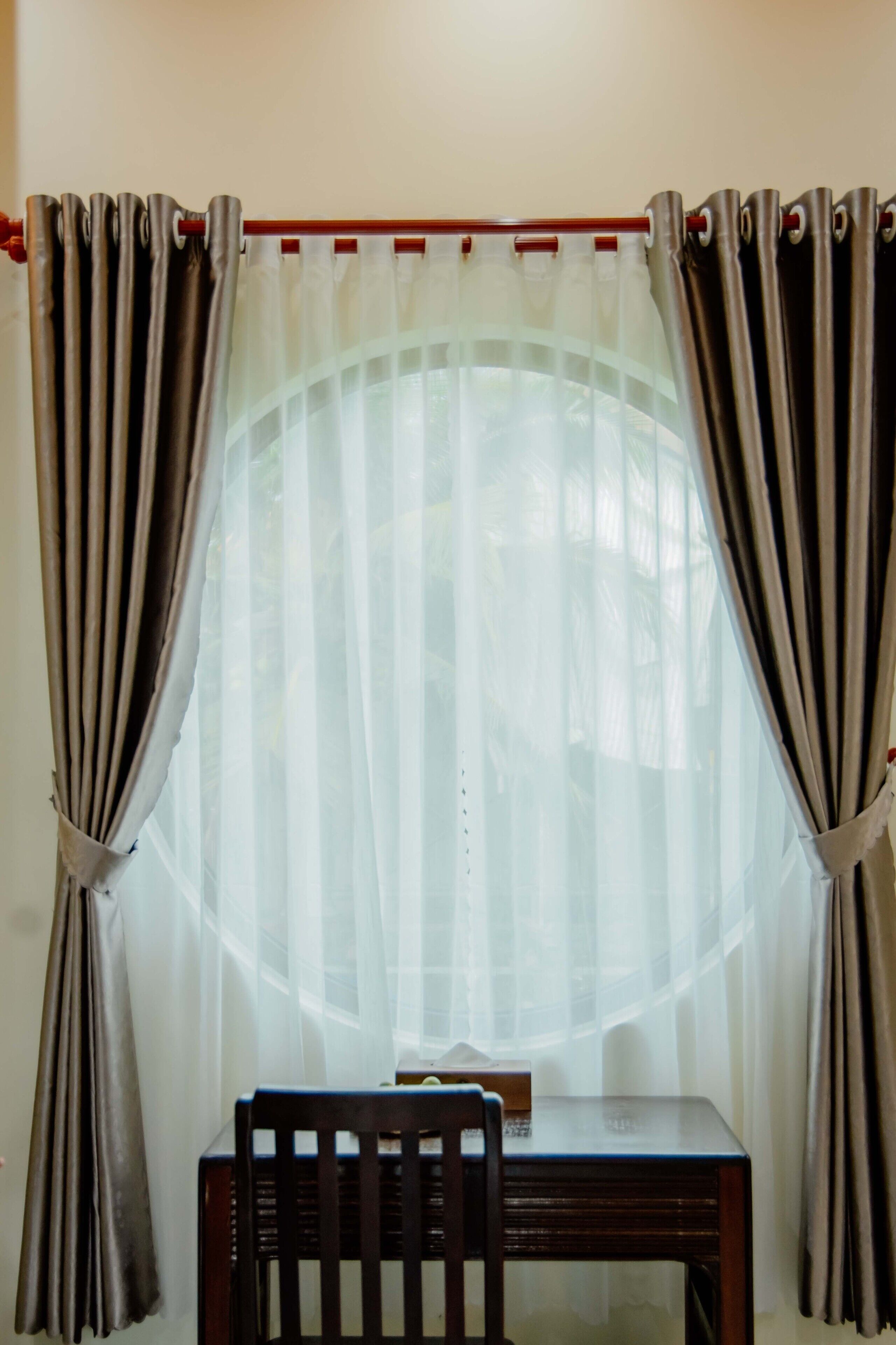 A room with a table and a chair, curtains, and a window with a view.