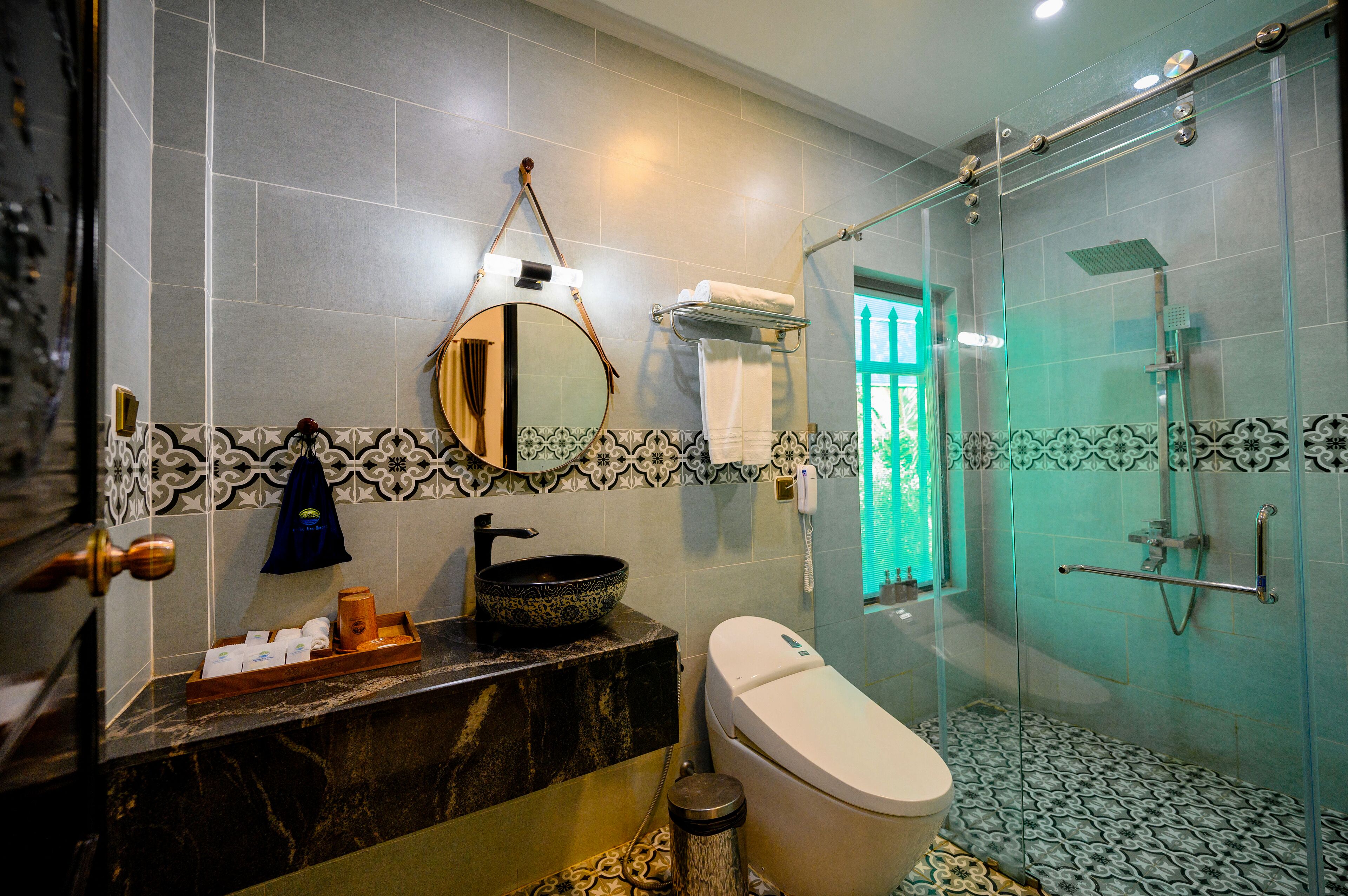 A bathroom with a marble sink, a toilet, a glass-enclosed shower, and a mirror with a hanging towel.