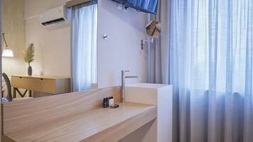 Un baño moderno con tocador de madera, un lavamanos blanco, un espejo y un televisor montado.