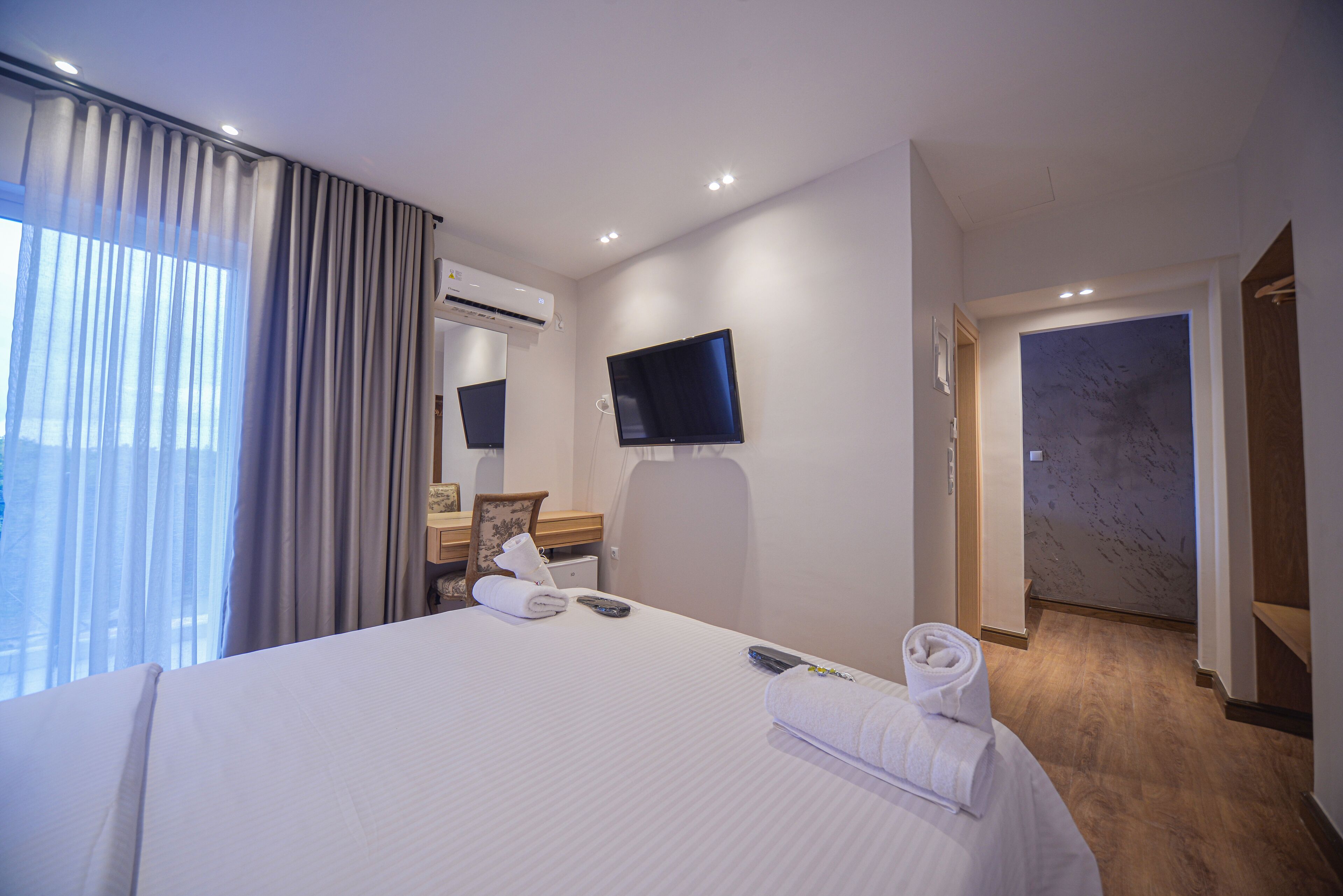 Una habitació d'hotel amb un llit gran, un televisor de pantalla plana fixat a la paret, una taula amb una cadira i una porta de bany.