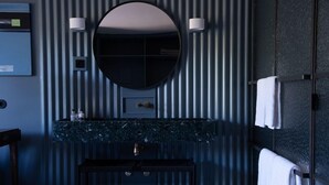 Un baño con espejo redondo, encimera de mármol, tocador negro y toallas en un escurridor.