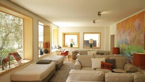 Amplia sala de estar con un gran sofá, una mesita y una silla. Grandes ventanales permiten la entrada de luz natural y vistas al exterior.