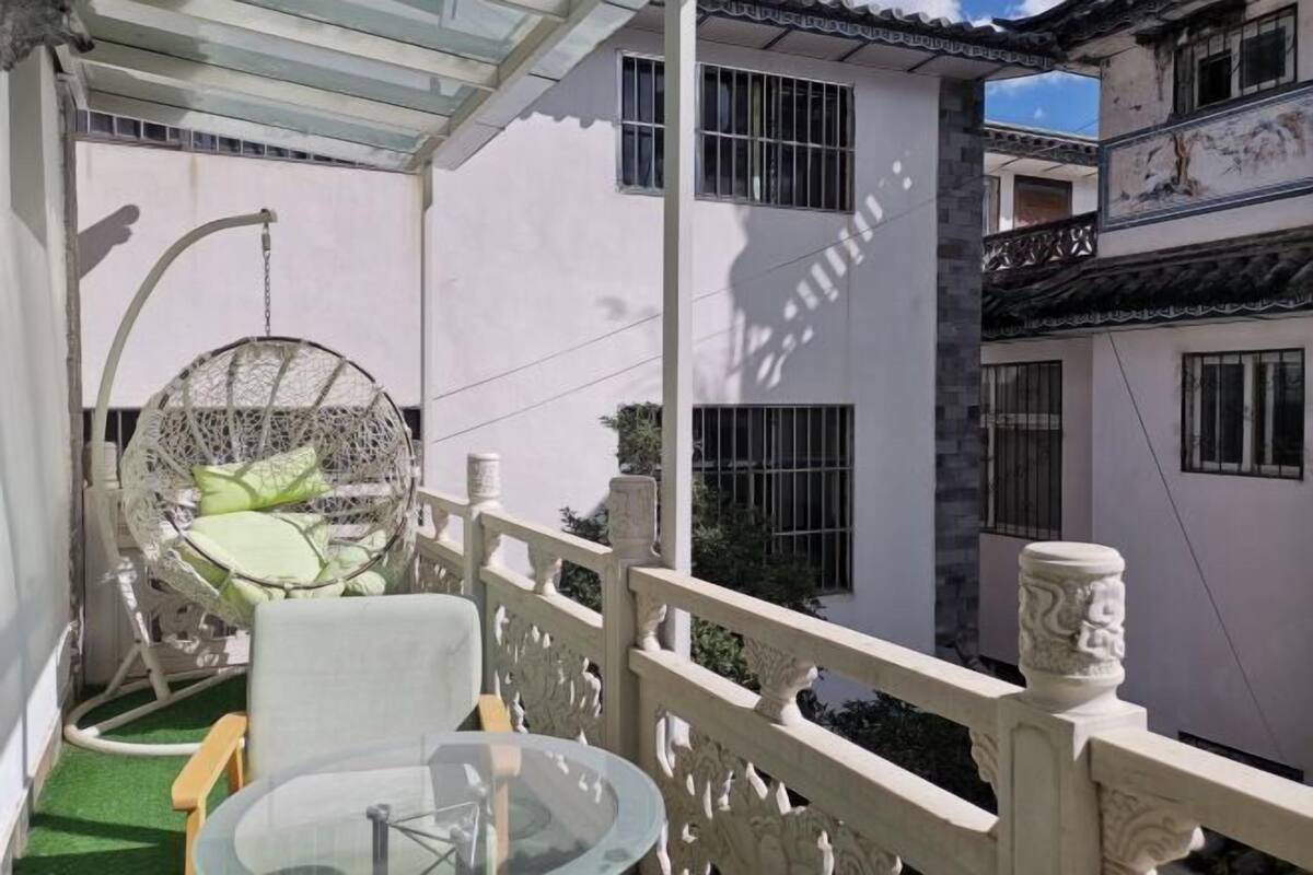 A balcony with a hanging chair, a glass table, and a white railing.