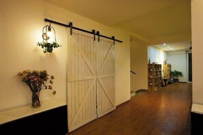 A hallway with a wooden floor, a white sliding barn door, a wall-mounted light fixture, and a vase with flowers. - Dali Ancient Town No. 204 Ideal Youth Hostel (Dali City)