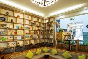 A library with bookshelves, a sofa with cushions, and a dining area with chairs. - Dali Ancient Town No. 204 Ideal Youth Hostel (Dali City)