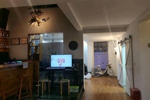 A living room with a wooden floor, a television, a bicycle, and a door leading to another room. - Dali Ancient Town No. 204 Ideal Youth Hostel (Dali City)