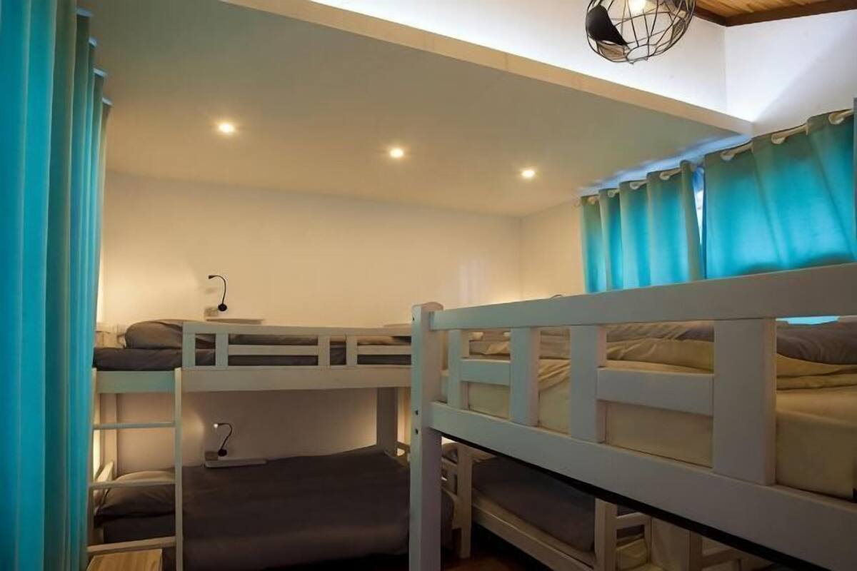 A bunk bed room with a desk, a lamp, and a window with curtains.